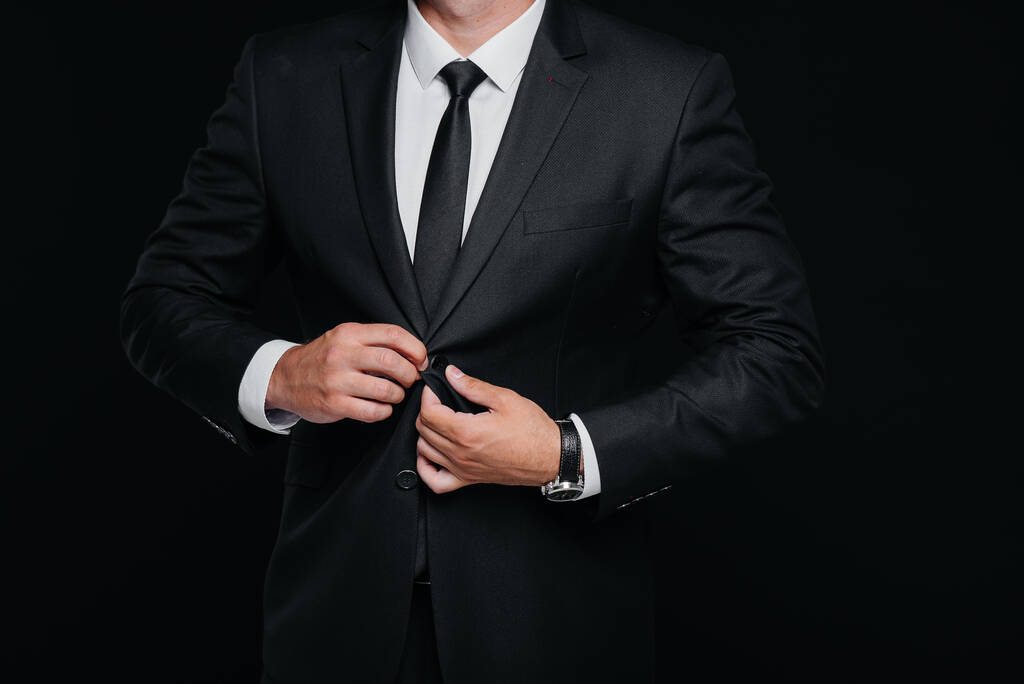 Egy jóképű fiatalember elegáns fekete öltönyt visel és fekete háttéren mosolyog. Takaríts fel, készülj.. - Fotó, kép