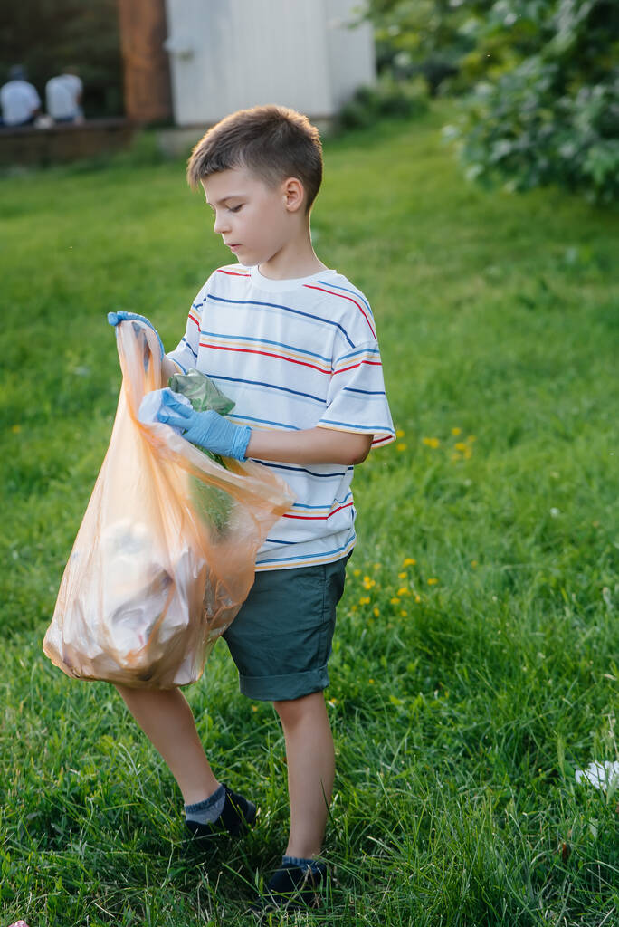 Egy hétéves kisfiú napnyugtakor szemetet gyűjt a parkban. Környezetvédelem, újrahasznosítás. - Fotó, kép