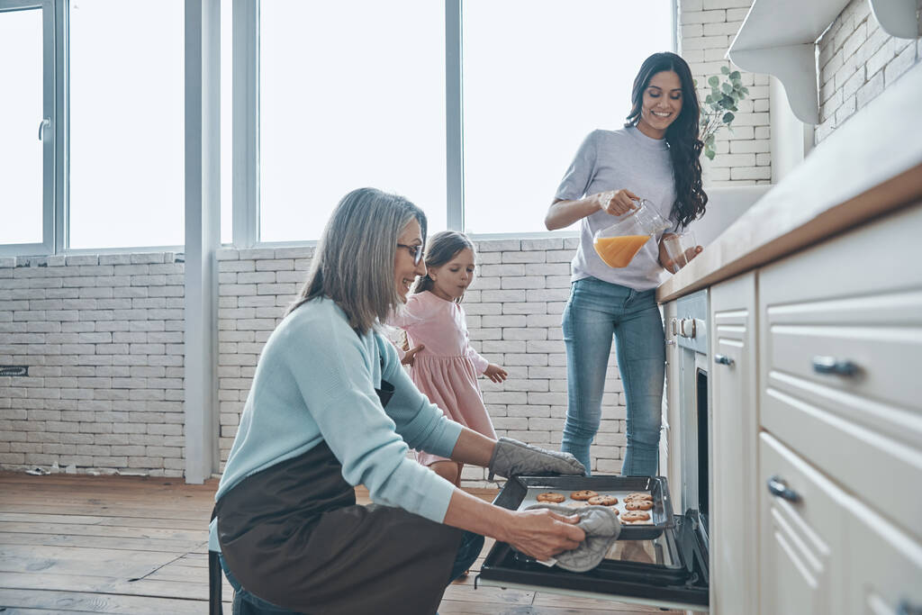 Glückliche Seniorin holt Plätzchen aus dem Ofen und lächelt, während sie Zeit mit der Familie verbringt - Foto, Bild