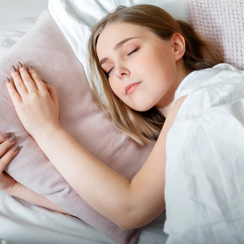 Chica adolescente en pijama duerme en el dormitorio por la mañana. Mujer joven durmiendo en la cama. Retrato de chica adolescente rubia tienen un buen sueño saludable en la almohada de color rosa blanco. cuadrado - Foto, Imagen