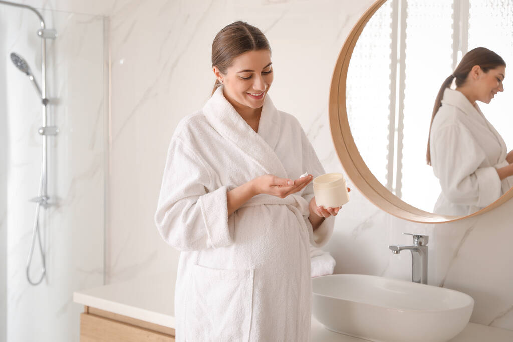 Jeune femme enceinte avec des produits cosmétiques dans la salle de bain - Photo, image