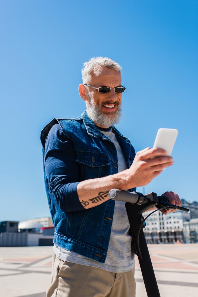щасливий чоловік в сонцезахисних окулярах використовує смартфон під час їзди на вулиці
  - Фото, зображення