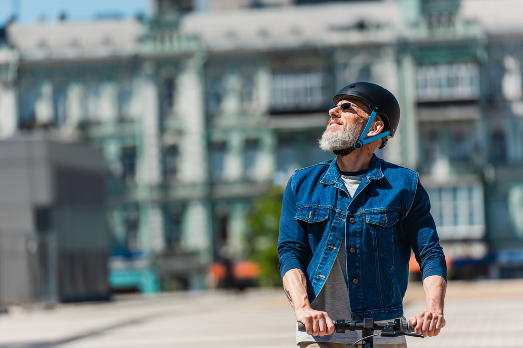 позитивный человек в солнцезащитных очках и шлеме на электронном скутере в городе  - Фото, изображение