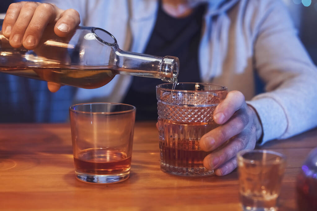 Starszy mężczyzna wlewa drinka do szklanki późnym wieczorem w domu, zbliżenie - Zdjęcie, obraz