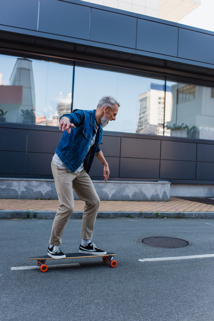 volle Länge der erstaunten und reifen Mann Reiten Longboard auf städtischen Straße - Foto, Bild