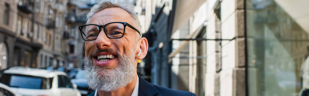 happy bearded man in glasses and earphones on urban street, banner - Photo, image