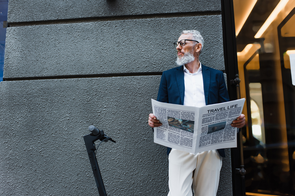 зрілий бізнесмен у блістері, що стоїть з газетою подорожей поблизу електронного скутера
  - Фото, зображення
