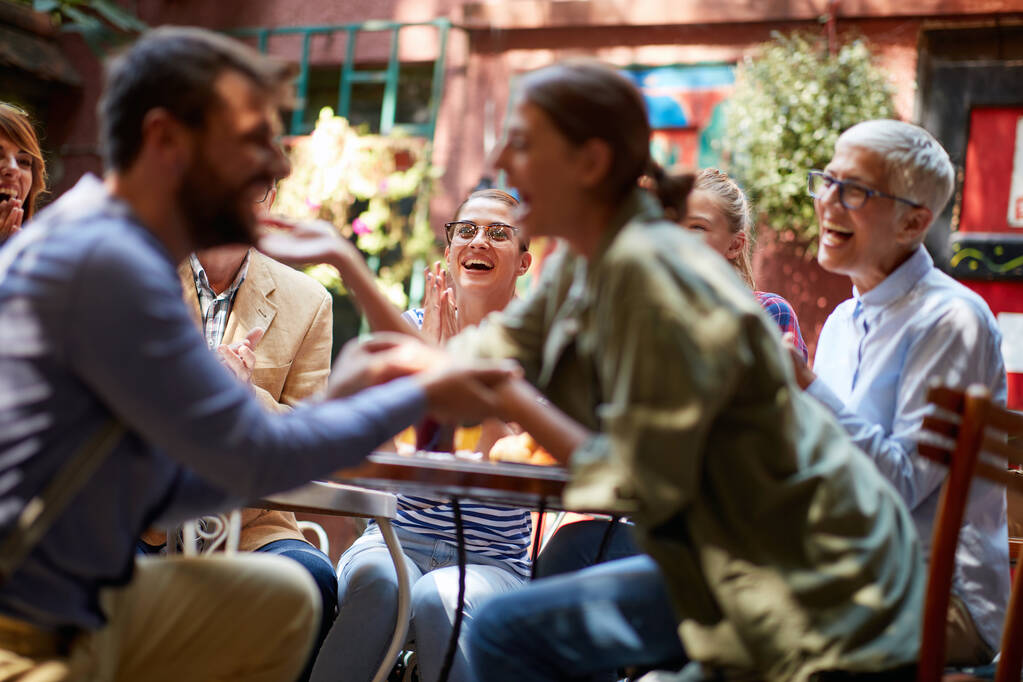 Een jonge man vraagt zijn vriendin ten huwelijk op een feestje in een vrolijke sfeer in een bar met vrienden. Vrije tijd, bar, liefde, buiten - Foto, afbeelding