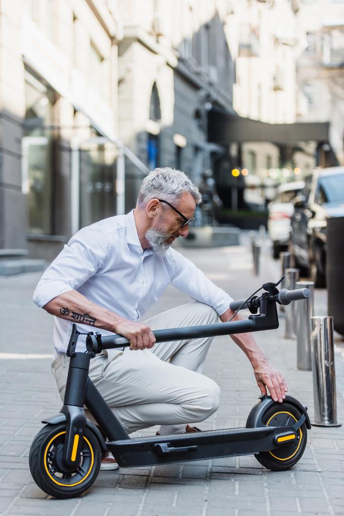mature man adjusting electric scooter on street  - Fotografie, Obrázek