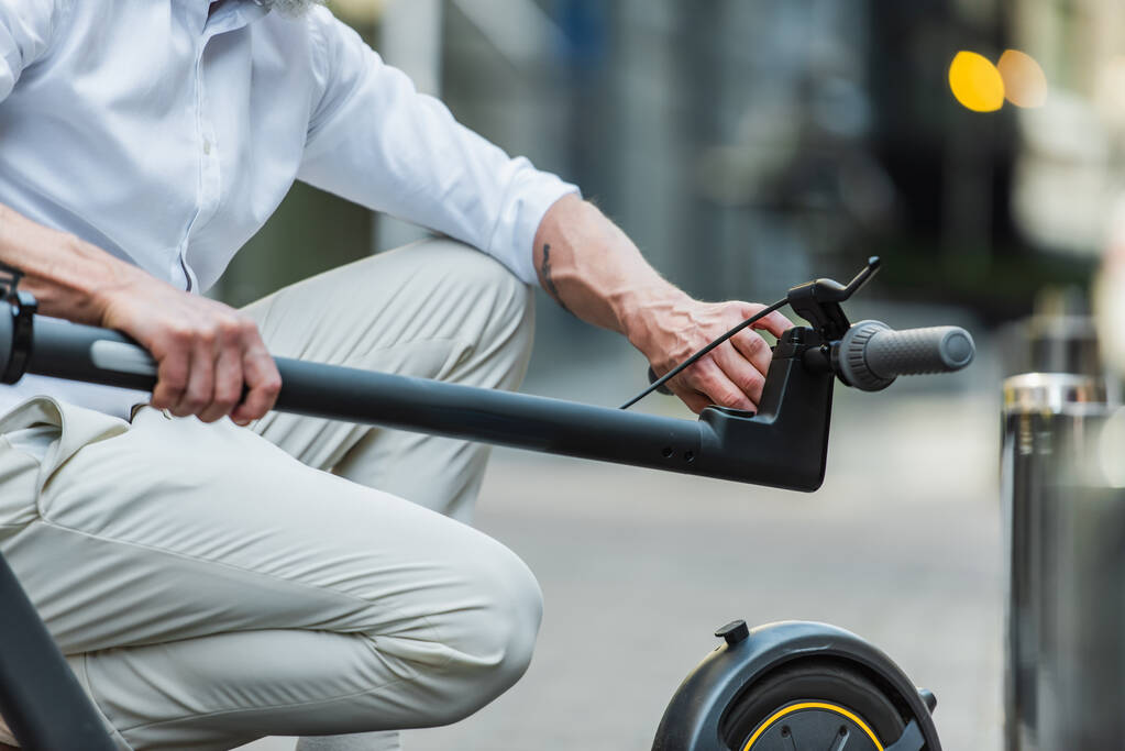 cropped view of mature man adjusting electric scooter on street  - Fotografie, Obrázek