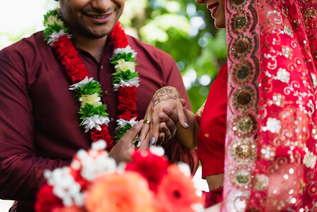 vista ritagliata dell'uomo indiano felice che indossa la fede nuziale al dito della sposa  - Foto, immagini