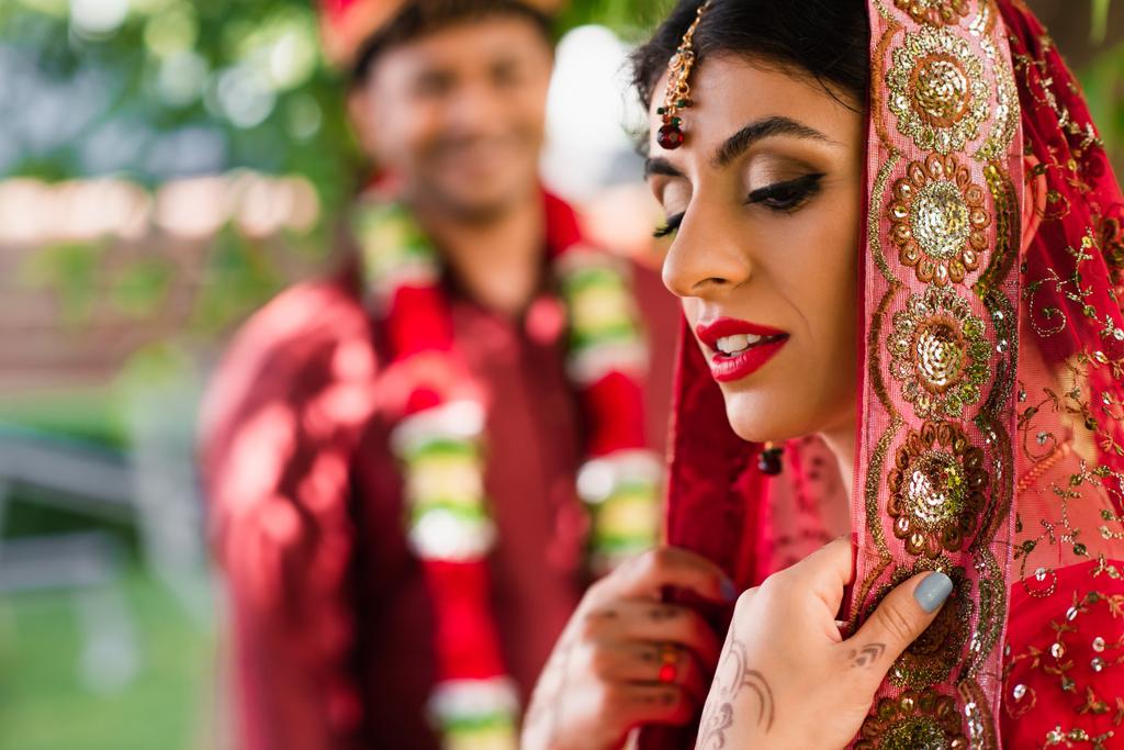 Indian bride in sari and headscarf near blurred man in turban on background  - Photo, Image