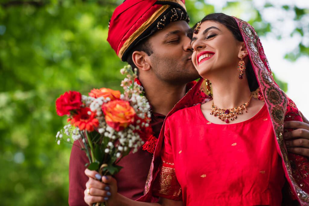 Ινδιάνος με τουρμπάνι φιλάει ευτυχισμένη νύφη με κόκκινο σάρι.  - Φωτογραφία, εικόνα