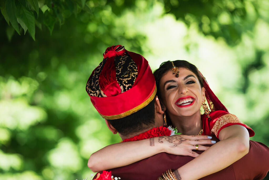 назад вид индийского мужчины в тюрбане обнимающего счастливую невесту в традиционном платке  - Фото, изображение