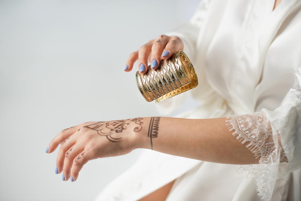 cropped view of indian woman with mehndi on hand wearing bracelet while getting ready to wedding isolated on white - Photo, Image
