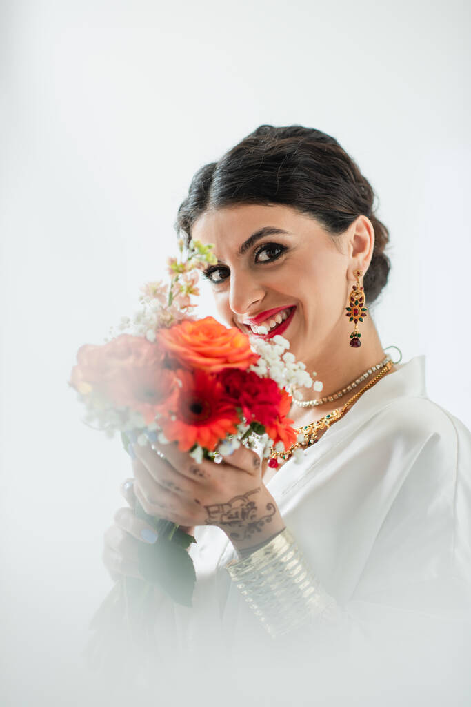 happy indian bride with mehndi holding bouquet of flowers on white - Photo, Image
