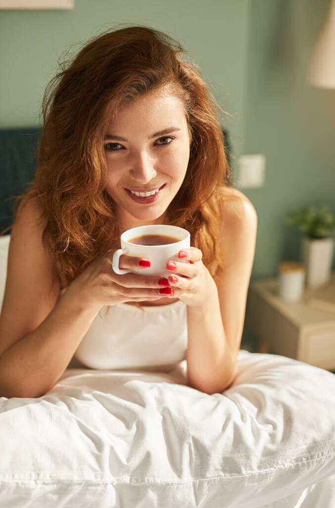 Happy woman drinking coffee in bed in morning - Photo, Image