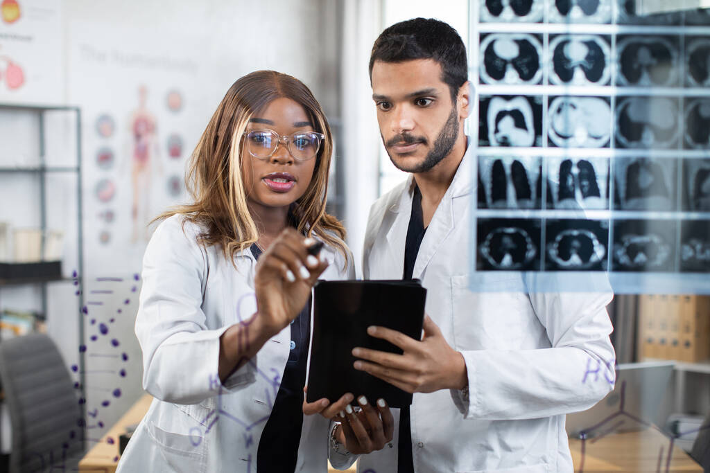 Врачи-мультирасовики изучают томографию пациента, стоящего у стеклянной стены - Фото, изображение