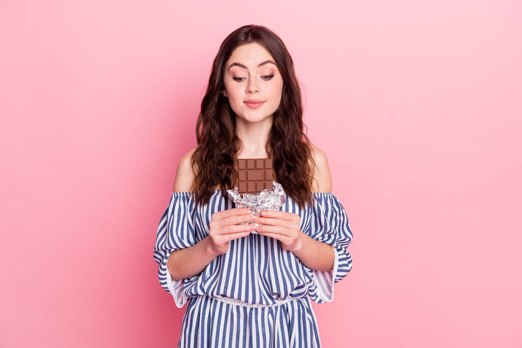 Fotografie pěkné optimistické brunetky dáma jíst čokoládové oblečení modré šaty izolované na růžovém pozadí - Fotografie, Obrázek