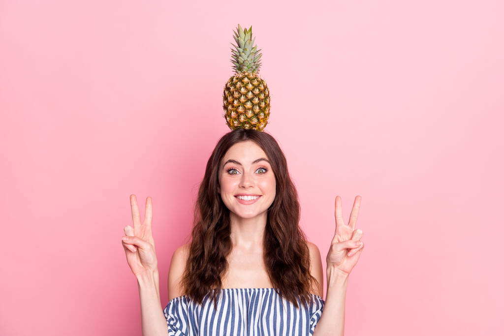 Fénykép aranyos édes fiatal hölgy kopás off-váll ruhák gazdaság fej ananász bemutató v-jelek izolált rózsaszín háttér - Fotó, kép