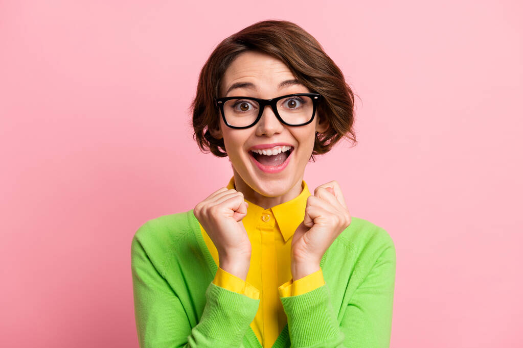 Φωτογραφία του τυχερού ενθουσιασμένοι νεαρή γυναίκα φορούν πράσινα γυαλιά ζακέτα ανοιχτό στόμα αυξάνεται γροθιές απομονωμένο παστέλ ροζ χρώμα φόντο - Φωτογραφία, εικόνα
