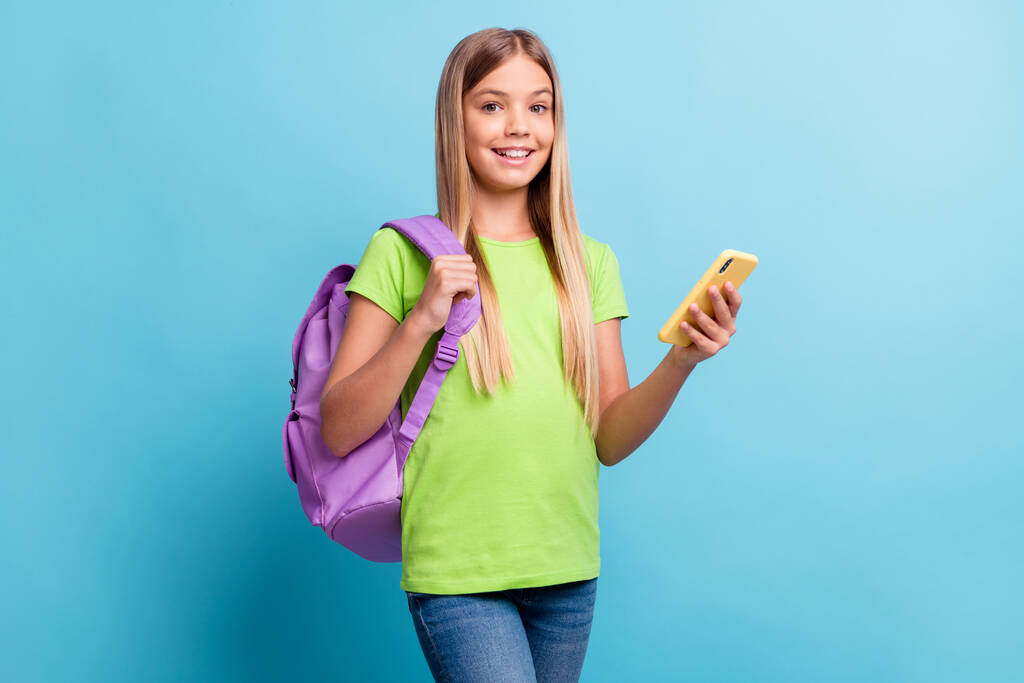 Photo de jeune souriant joyeuse bonne humeur positive fille blogueur en utilisant le téléphone porter sac violet isolé sur fond de couleur bleue - Photo, image