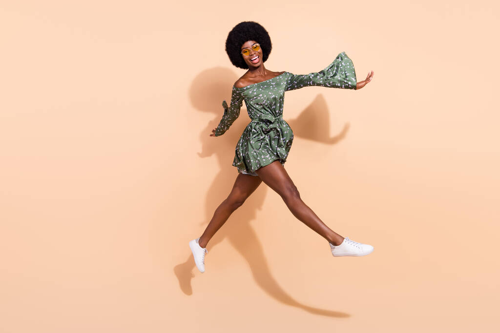 Full length profil boční fotografie mladé vzrušené černošky dívka šťastný pozitivní úsměv jít chůze krok skok izolované přes béžové barvy pozadí - Fotografie, Obrázek