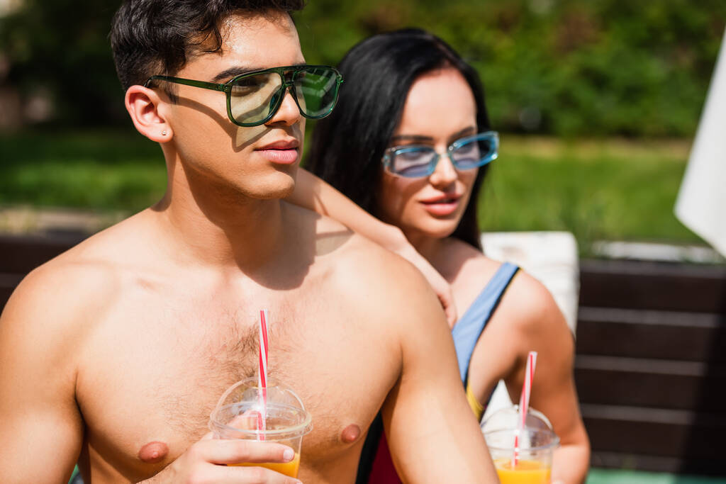 Bulanık kız arkadaşının yanında elinde portakal suyu tutan gömleksiz bir adam.  - Fotoğraf, Görsel
