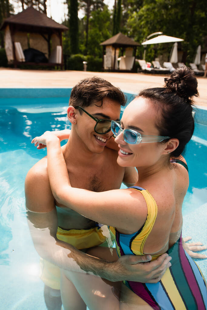 Νεαρό ζευγάρι με κλειστά μάτια αγκαλιάζει στην πισίνα στο θέρετρο  - Φωτογραφία, εικόνα