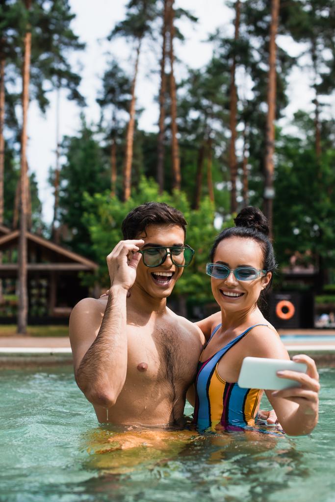 Gelukkig paar in zonnebril selfie op smartphone in het zwembad tijdens het weekend  - Foto, afbeelding