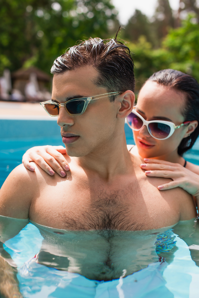 Donna sfocata in occhiali da sole abbracciare fidanzato in piscina  - Foto, immagini
