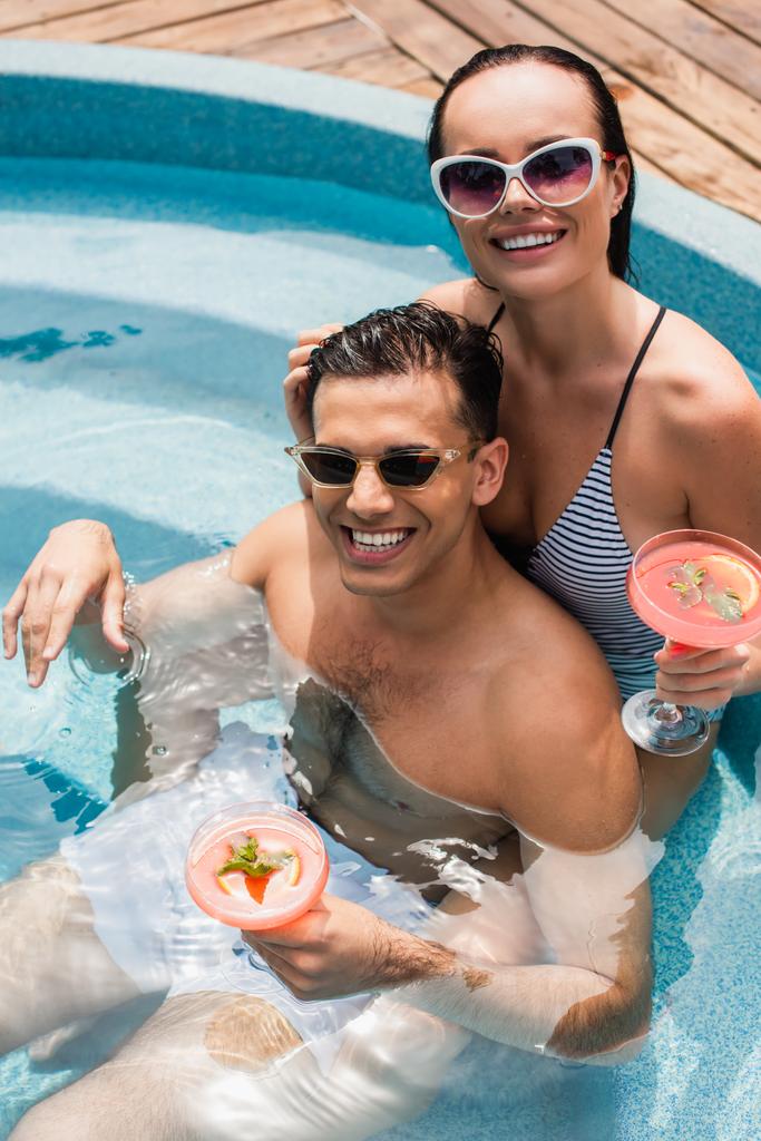 High angle view of cheerful couple holding cocktails in swimming pool  - Photo, Image