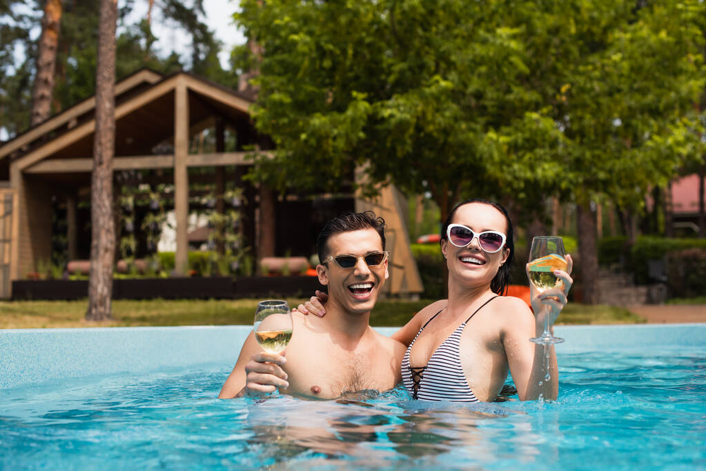Giovane coppia che tiene bicchieri di vino bianco in piscina  - Foto, immagini