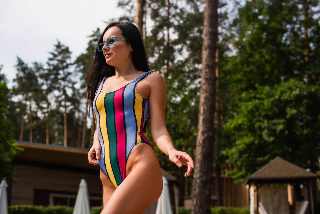 Low angle view of brunette woman in swimwear standing outdoors  - Photo, Image