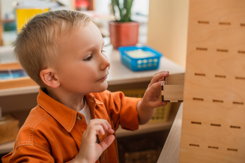 Kind öffnet Schrank in Holzkiste beim kognitiven Spiel in Montessori-Schule - Foto, Bild