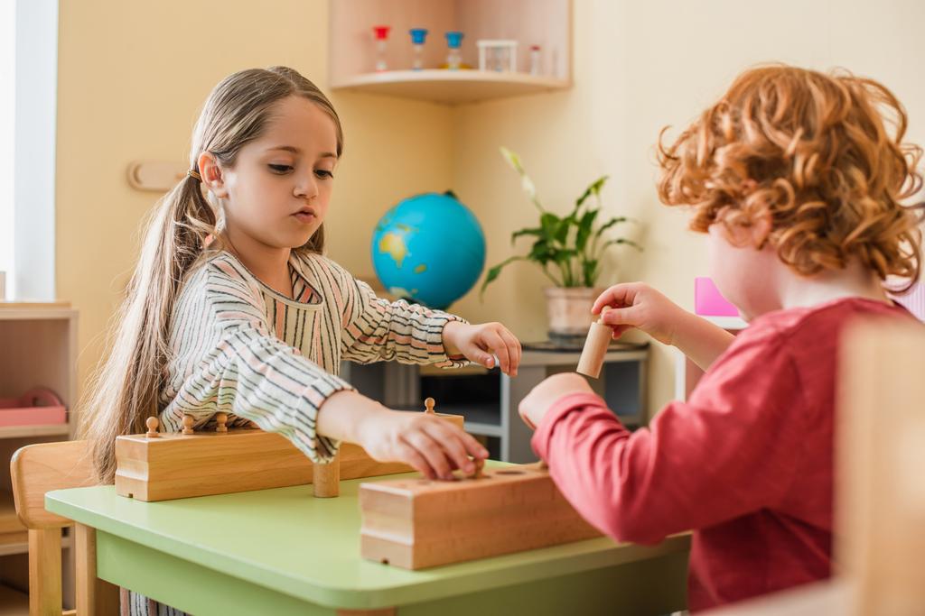blurred redhead boy playing cognitive game with girl in montessori school - Photo, Image