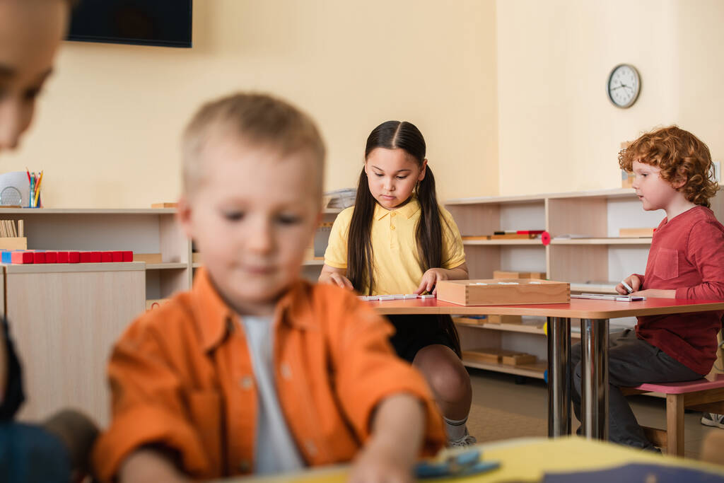niños interracial jugando juego educativo cerca de niño y profesor en primer plano borrosa - Foto, Imagen