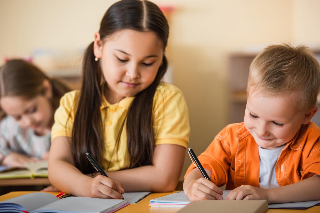 πολυεθνικά παιδιά που γράφουν σε βιβλία αντιγράφων κατά τη διάρκεια του μαθήματος στο σχολείο Montessori - Φωτογραφία, εικόνα