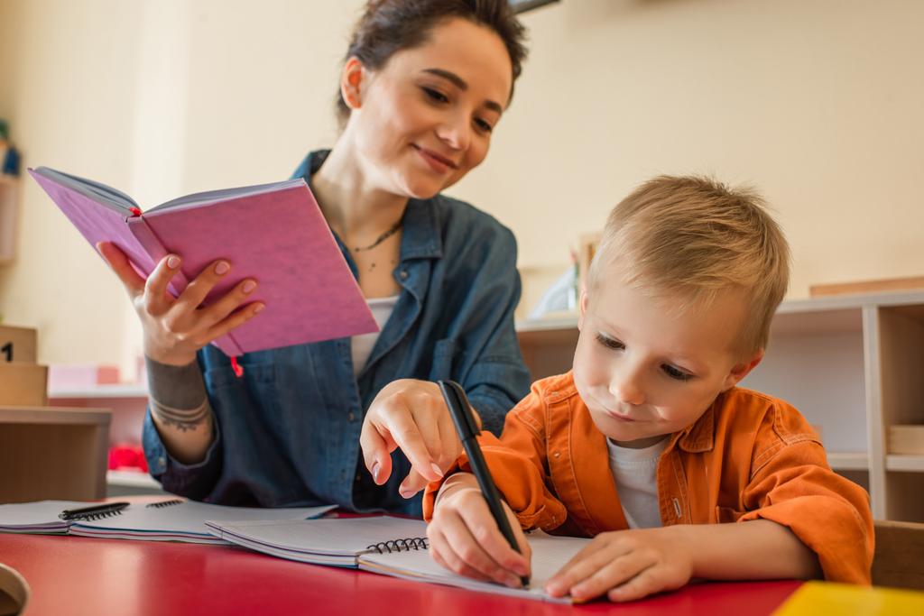 mosolygós tanár ujjal mutogat a gyerek közelében írás diktálás a montessori iskolában - Fotó, kép