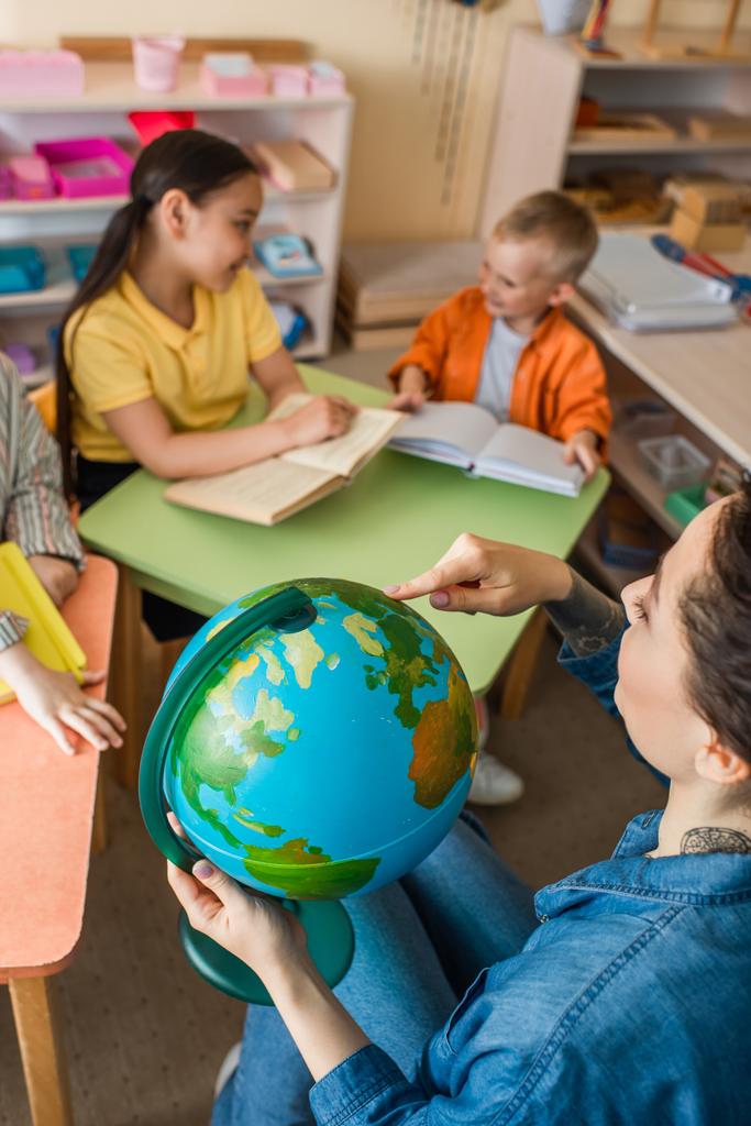 hoge hoek uitzicht van de leraar wijzen op globe in de buurt multi-etnische kinderen tijdens de les - Foto, afbeelding