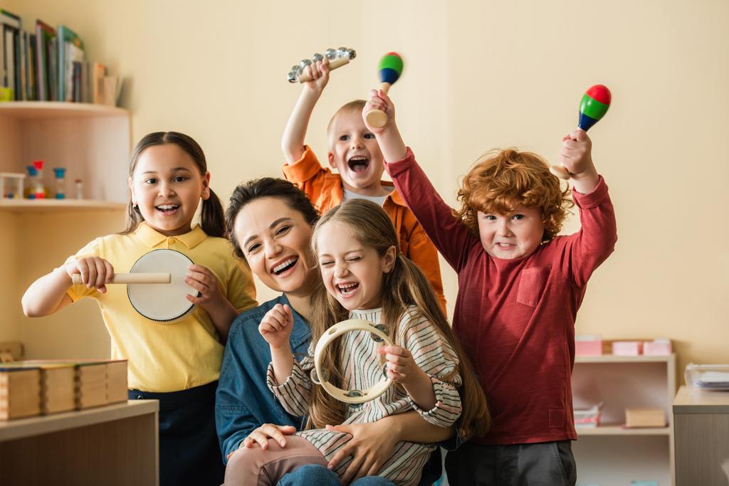 vzrušené multietnické děti hrající na hudební nástroje poblíž šťastný učitel - Fotografie, Obrázek