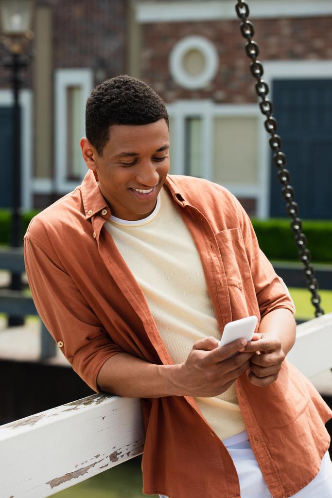веселий афроамериканський чоловік використовує мобільний телефон на міському мосту
 - Фото, зображення