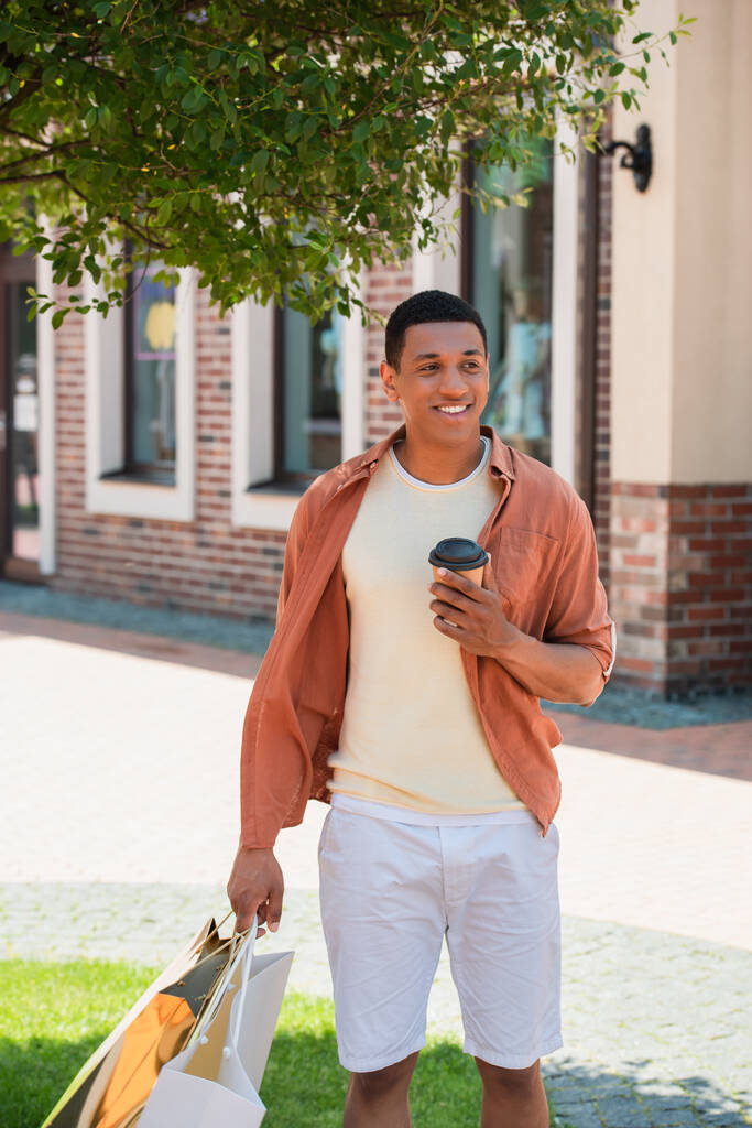 glücklich afrikanisch-amerikanischer Mann mit Imbissgetränk zu Fuß mit Einkaufstüten in der Stadt - Foto, Bild