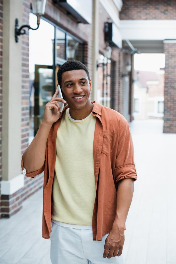 jong Afrikaans amerikaans man glimlachen terwijl praten op mobiele telefoon op straat - Foto, afbeelding