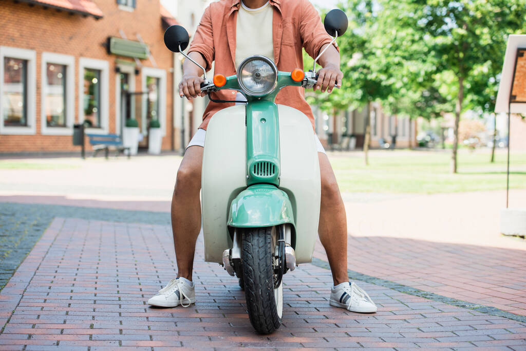 Ausgeschnittene Ansicht eines Afroamerikaners auf einem Motorroller im Freien - Foto, Bild