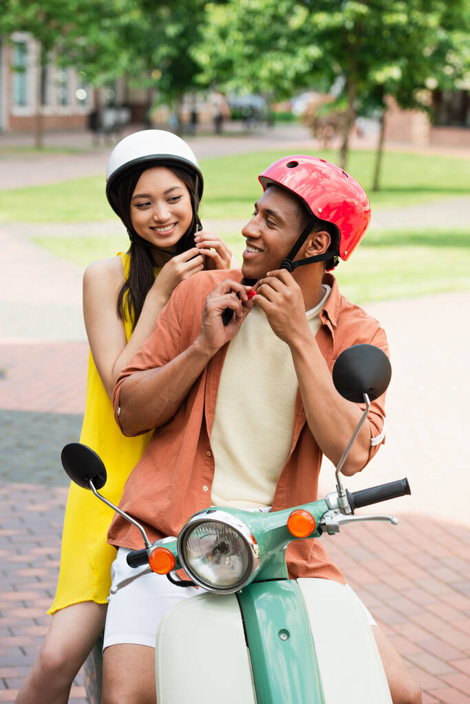 веселые межрасовые пары крепят защитные шлемы перед поездкой на скутере - Фото, изображение
