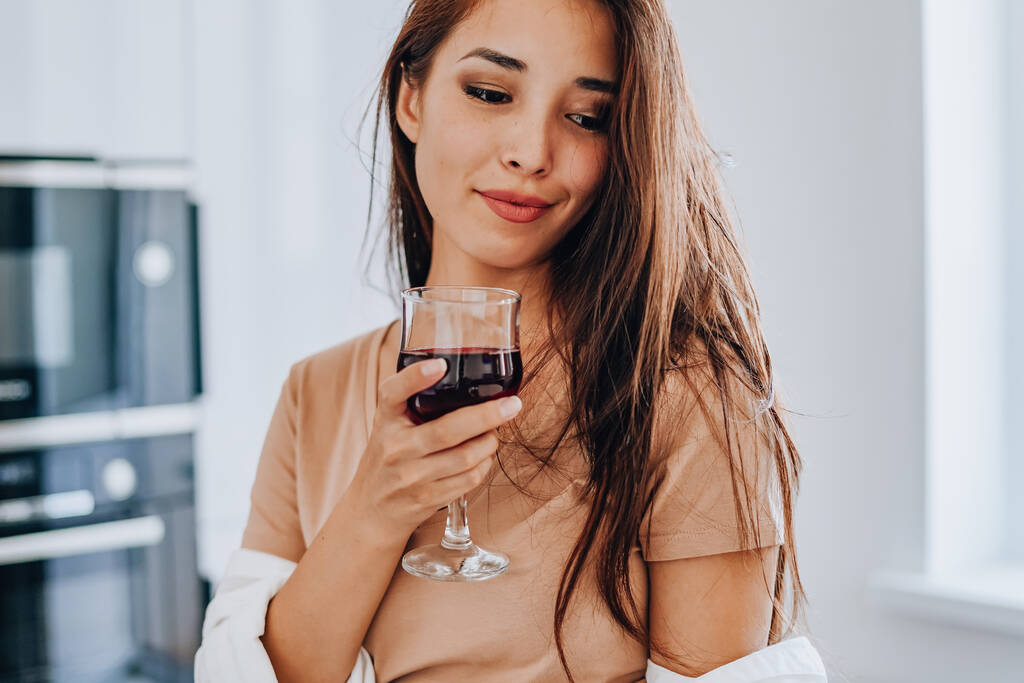 donna asiatica bere vino in cucina a casa - Foto, immagini