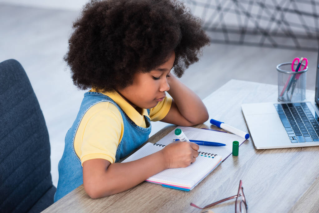 アフリカ系アメリカ人の子供がノートパソコンで自宅で書いている様子  - 写真・画像