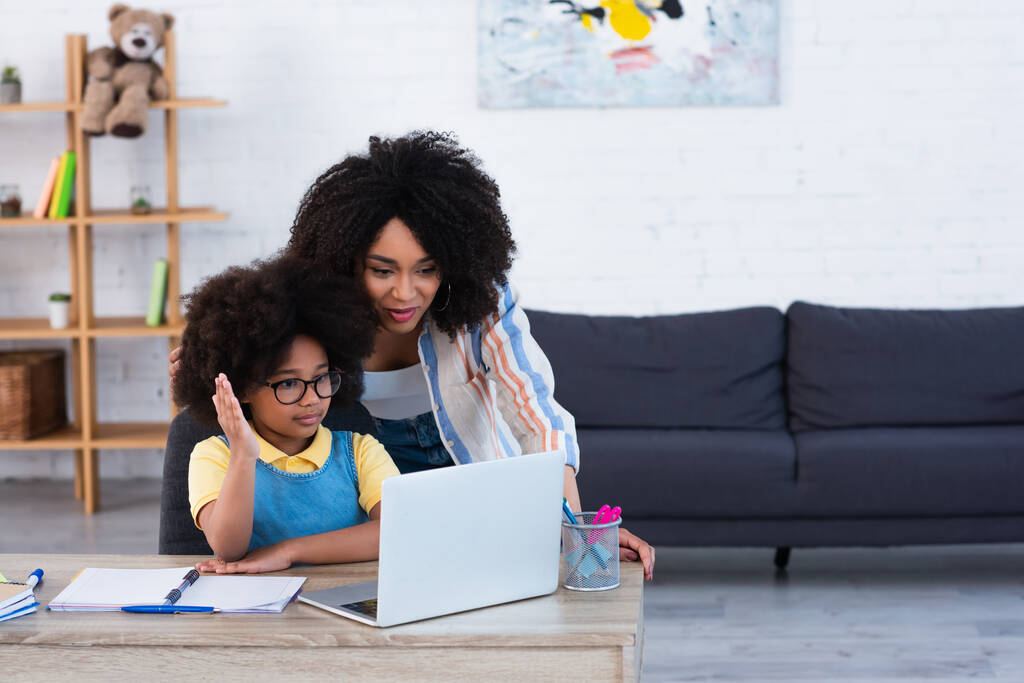 Afrikai amerikai gyerek felemeli a kezét közelében laptop és anya otthon  - Fotó, kép