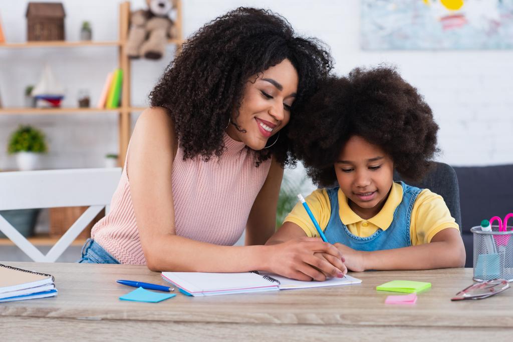 Mosolygó afro-amerikai anya ír a notebook a gyerek otthon  - Fotó, kép